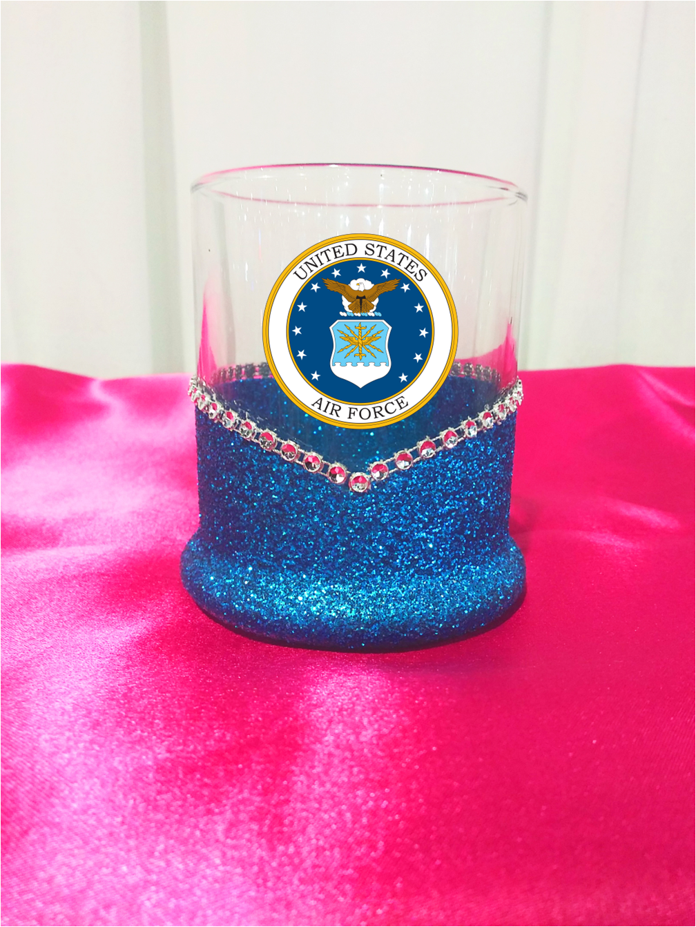 Clear Whiskey highball glass with blue glitter base and Air Force emblem on a pink surface