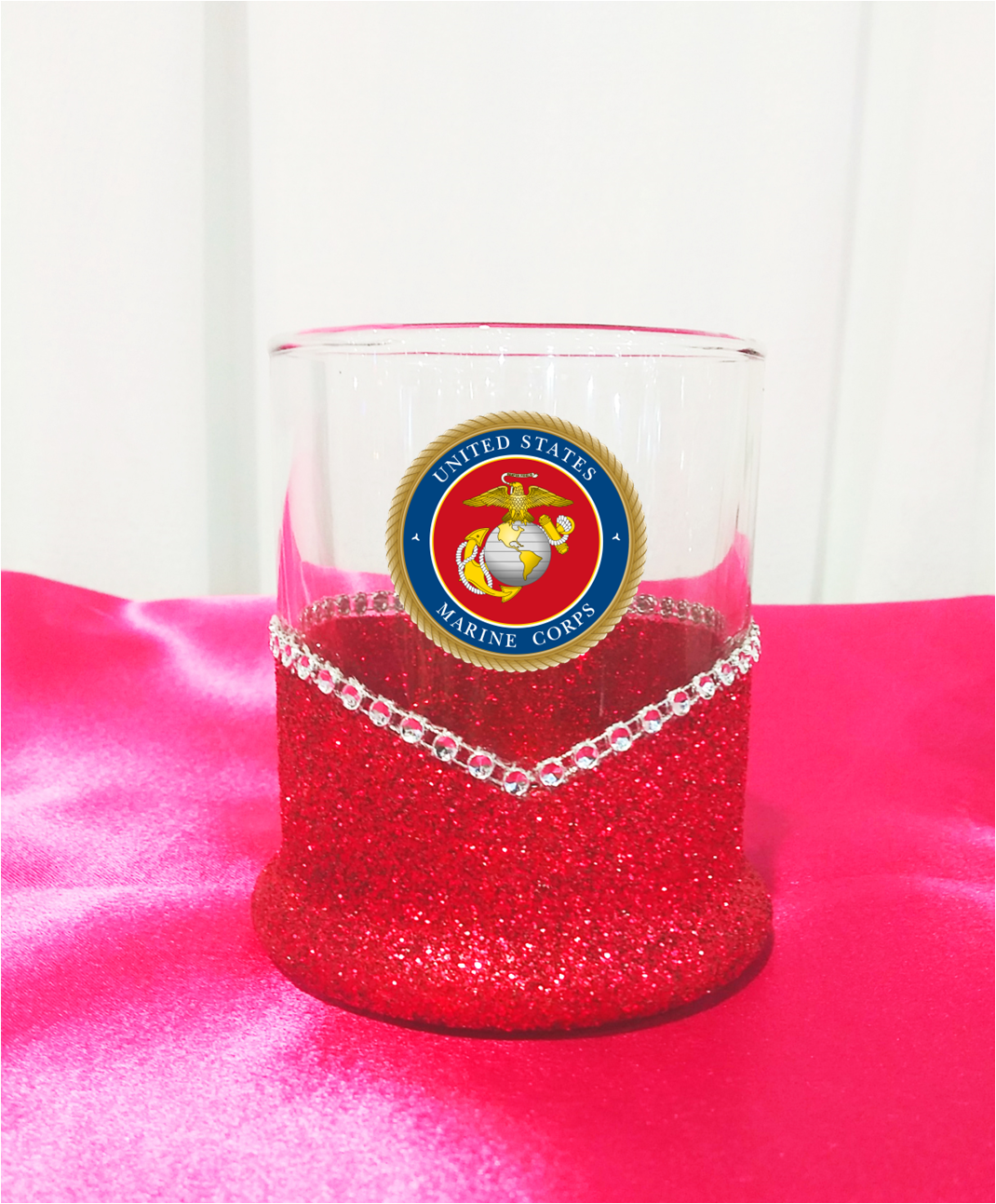 Whiskey highball Glass tumbler with red glittery base and US Marine Corps emblem on a pink surface